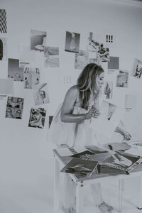 ALT: Grace standing over a table with client project papers scattered all over in black and white