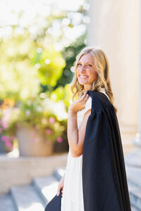 senior in white dress with black cap and gown smiling about her achievement