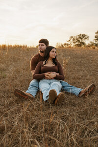 Couples sitting together in a golden farm field during a fall sunset couples session in Aiken SC.