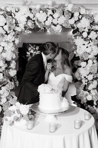 bride and groom kissing while cutting wedding cake