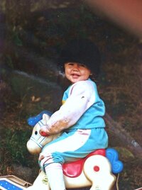 Hiliary as a toddler sitting on toy rocking horse wearing a riding helmet