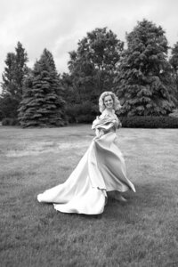 Black and white photo of a woman in an elegant gown twirling her dress in a grassy field