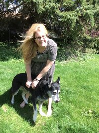 smiling woman stands in grass petting dog