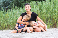Tarzan sits on a beach in the sand, her two children gathered up on her lap snuggling each other