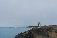 Two women embrace on a mountain edge near the water in Iceland