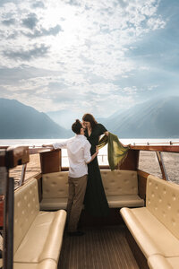 a couple kissing on a boat with lake como mountains of italy in the background