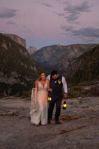 Newlyweds walk in the fading light with lanterns  in Yosemite, Halfdome and El Cap in the background.