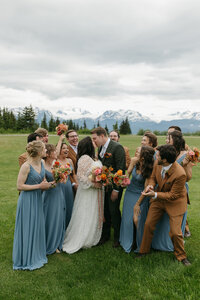 A bridal party surrounding the couple while they kiss. 