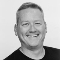 A black and white photo of Adam from Gamably, smiling warmly at the camera, radiating joy and positivity.