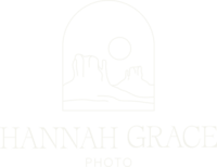 A white version of the Hannah Grace Photo logo. The Logo feautres a delicate handdrawn illustration of 2 buttes and the sun encased in an arch