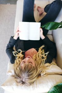 A woman sits on a couch with a book in hand, reflecting on her therapy journey and feelings of being stuck.