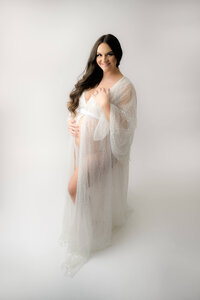 Maternity  photo session with mom to be wearing a sequin beaded white robe photographed with a white background. Image by E. Benecki Photography