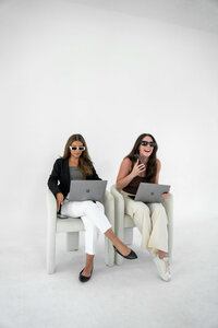 Two women laughing with computers in a white studio room