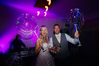 bride and groom hold light up balloons in the air as they stand in the purple lit party room at their ibiza style wedding party at Swallows Nest wedding barn