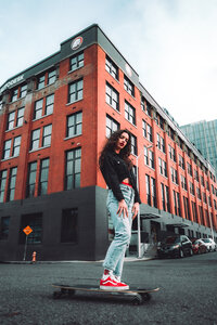 oung entrepreneur with skateboard poses on city street in front of industrial red building – brand photo by Mewphotovideo for modern creatives