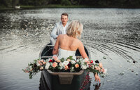 a bride and groom in a canoe together with the bride reaching one hand into the water