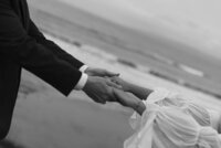 Black and white detail photo of bride and groom holding hands.
