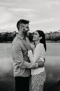 engaged couple hugging and laughing by the water in black and white