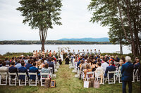 A wedding ceremony with a mountain and lake as their backdrop with all their guests seated in front.
