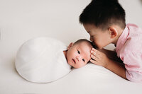 In-studio portrait of boy kissing wrapped newborn baby