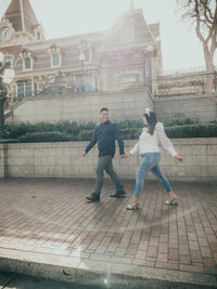 A couple walking hand-in-hand during their engagement photoshoot at Disneyland.