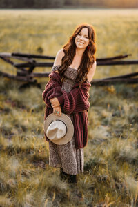 Owner Annie Bee Photography in a field at sunset wearing a maxi dress and oversized sweater in Flagstaff.