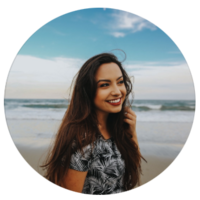 A professional headshot of a brunette woman smiling at the beach.