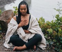 A woman sits with hands on her chest and belly, representing the integration of breathing and yoga in the journey of self growth,.