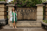 A graduate poses proudly next to the Colorado State University sign in Fort Collins, Colorado. The iconic CSU sign serves as a memorable backdrop for this celebratory moment, marking the achievement of graduation.