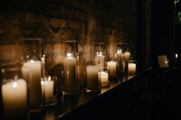 Dimly lit hallway lined by candles illuminating brick wall