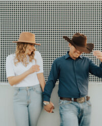 couple holds hand with hats