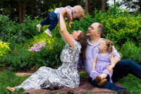 A mom holding up a baby with dad and small child sitting next to her