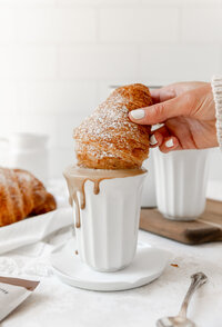 a croissant being dipped into hot chocolate