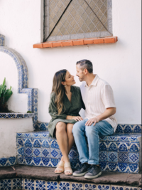 Natalie Bernacchi sitting with her husband on a tiled bench, sharing a warm moment outside a white Spanish-style building