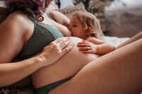 close up of mom and daughter hands on mom's pregnant belly while she breastfeeds daughter