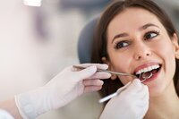 A woman smiling in dental chair with dental tools in her mouth