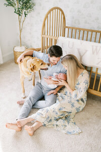 New parents hold newborn baby boy while dog comes over to say hello during in-home photoshoot