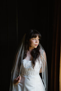 moody photo of bride looking out a window for her portraits