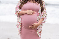 Close up of a pregnant woman in a pink dress holding her belly