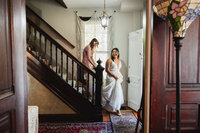 A bride walking down the stairs as someone holds the back of their train 