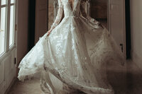 Close-up of a bride twirling in a lace long-sleeve gown in soft window light.