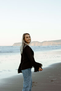 Karli Fisco of Karli Anne Films waring a black top and blue jeans dancing on a washington beach