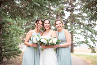 A bride stands with her bridesmaids in some trees.
