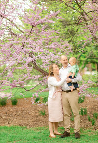 Mom and Dad playing with their baby son under a flowering redbud tree