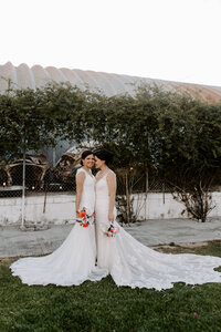A newlywed couple standing close together smiling and holding bouquets of flowers 
