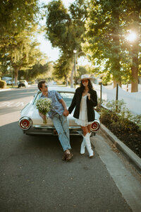 man and woman holding hands while leaning against a classic car