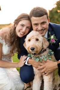 Wedding Couple smiles with goldendoodle at sunset