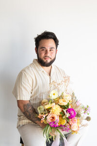 An Austin wedding photographer captures a man sitting on a chair with a bouquet of flowers.