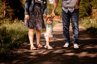In the background there's a jade color wall with a white crib. Mom stands in front of crib in a close up shot while she holds the newborn baby and touches noses while smiling. Mom is in a black and white stripe dress and baby is in a white long sleeve outfit with a flower headband.