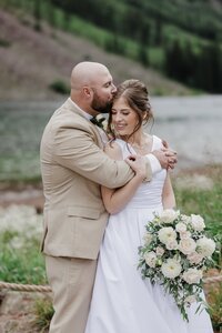 Wedding and Elopement Photography,  bride and groom embrace in front of alpine lake during Rocky Mountain elopement.